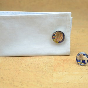May include: A pair of cufflinks featuring a silver-toned design with a blue background. One cufflink depicts a portrait of a Native American man, while the other cufflink depicts a buffalo. The text "FIVE CENTS" is visible on the buffalo cufflink.