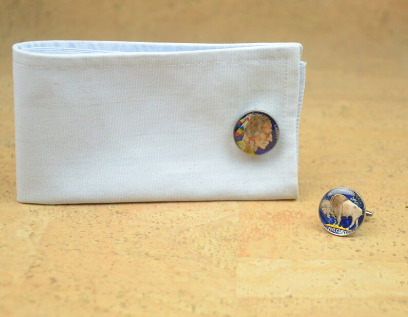 May include: A pair of cufflinks featuring a silver-toned design with a blue background. One cufflink depicts a portrait of a Native American man, while the other cufflink depicts a buffalo. The text "FIVE CENTS" is visible on the buffalo cufflink.
