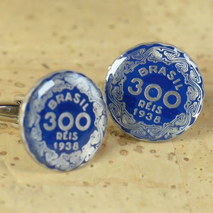 May include: A pair of cufflinks featuring a blue enamel design with silver accents. The cufflinks are round and feature the text "BRASIL 300 REIS 1938".