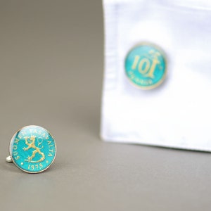 Pode incluir: Um par de bot&otilde;es de punho com uma moeda azul-esverdeada e dourada com um desenho de le&atilde;o. A moeda diz "SUOMEN TASAVALTA 1975".