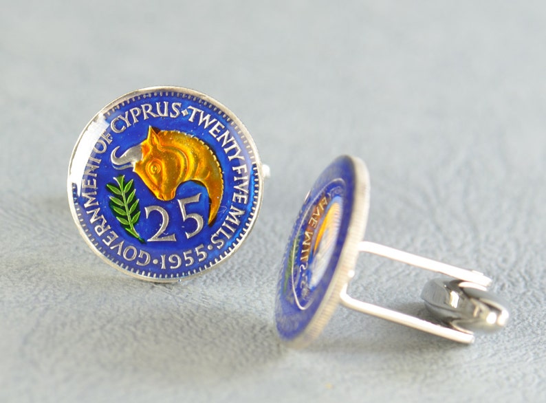 Peut inclure: Une paire de boutons de manchette en pi&egrave;ces de monnaie vintage de 25 mils chypriotes. Les pi&egrave;ces pr&eacute;sentent un fond bleu avec un taureau dor&eacute; et une branche d'olivier verte. Le texte "GOVERNMENT OF CYPRUS TWENTY FIVE MILS 1955" est inscrit sur le bord de la pi&egrave;ce.