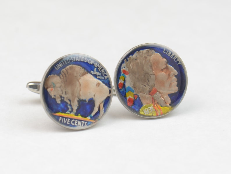 May include: A pair of cufflinks featuring a vintage American Indian Head nickel and a vintage Buffalo nickel. The coins are painted with blue, red, yellow, and white accents. The Indian Head nickel features the text "LIBERTY" and the Buffalo nickel features the text "UNITED STATES OF AMERICA" and "FIVE CENTS".