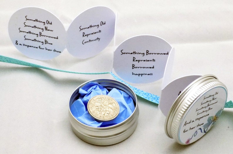 Puede incluir: Una lata de plata con una tapa de dise&ntilde;o azul y blanco que contiene una moneda de seis peniques. La tapa tiene el texto "Something Old, Something New, Something Borrowed, Something Blue & a sixpence for her shoe". Hay tres tarjetas blancas con texto en ellas: "Something Old Represents Continuity", "Something Borrowed Represents Borrowed Happiness", y "Something Borrowed Represents Borrowed Happiness".
