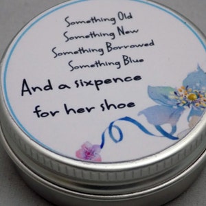 Puede incluir: Una lata de plata con una etiqueta blanca que dice "Something Old, Something New, Something Borrowed, Something Blue, And a sixpence for her shoe". La etiqueta tambi&eacute;n tiene una flor azul con un centro amarillo.