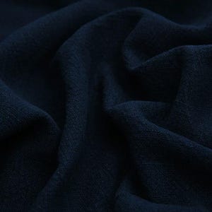 May include: A dark navy blue fabric with a visible knit texture, featuring deep folds and soft shadows that create a draped effect across the surface. The material displays a consistent, dense weave pattern throughout the entire composition.