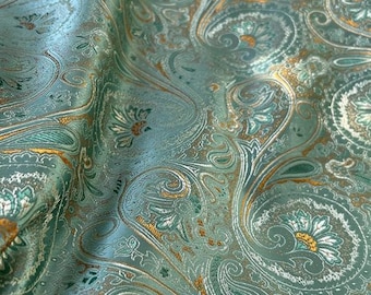 May include: Teal fabric with a paisley pattern in gold and white. The fabric has a subtle sheen and a textured surface.