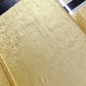 Peut inclure: Un tissu doré à motif de roses. Le tissu a un léger brillant et une surface texturée.