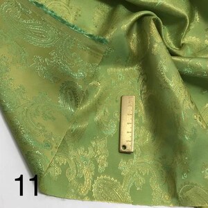 May include: Green paisley fabric with a gold metallic sheen. The fabric is folded and a ruler is placed on top of it. The number "11" is written in the bottom left corner of the image.