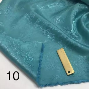 May include: Teal paisley patterned fabric with a gold-colored ruler measuring 10 inches.
