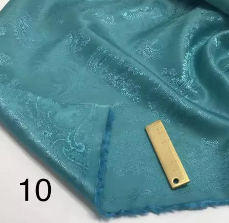 May include: Teal paisley patterned fabric with a gold-colored ruler measuring 10 inches.