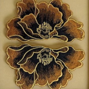 Puede incluir: Dos parches de tela bordados en forma de peonías. Los parches son negros y dorados con un diseño detallado.