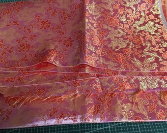 Könnte beinhalten: Rosafarbener Stoff mit einem roten und goldenen Blumendesign. Der Stoff ist in mehreren Schichten gefaltet und hat eine seidige Textur.