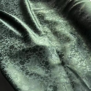 May include: Green fabric with a subtle embossed pattern of stylized flowers and leaves. The fabric has a soft, silky texture.