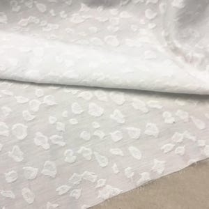 Könnte beinhalten: Weißer Stoff mit einem geprägten Leopardenmuster. Der Stoff ist weich und texturiert.