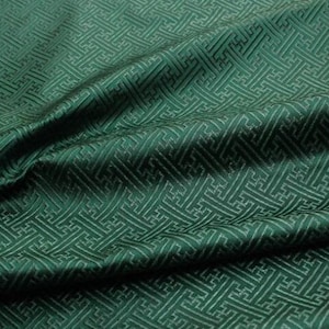 May include: Green fabric with a white geometric pattern. The fabric is folded and has a soft, silky texture.