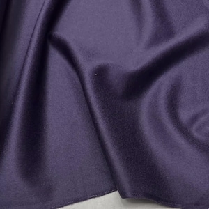 May include: A close-up shot of a deep purple fabric, showing soft folds and a gentle sheen. The material appears smooth and drapes gracefully, with shadows creating depth. The fabric's colour is a rich, dark shade of purple.