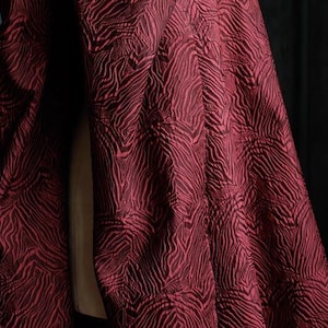 Könnte beinhalten: Nahaufnahme eines roten Stoffes mit einem schwarz-roten Zebra-Muster. Der Stoff hat eine strukturierte, gesteppte Optik.