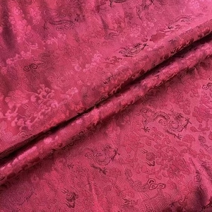 May include: Red fabric with a raised pattern of dragons and clouds. The fabric is soft and silky.