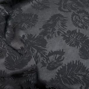 May include: A dark charcoal gray fabric featuring a repeating pattern of matte black tropical leaves. The material displays a subtle contrast between the textured, raised leaf motifs and the smoother, slightly lighter background surface.