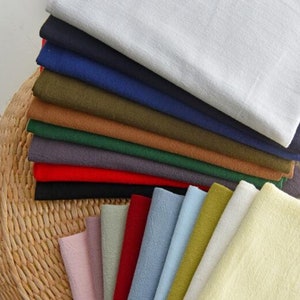 May include: A stack of fabric swatches in various colors, including white, navy blue, olive green, brown, green, gray, red, and black. The swatches are arranged in a fan shape, with the lighter colors at the top and the darker colors at the bottom.