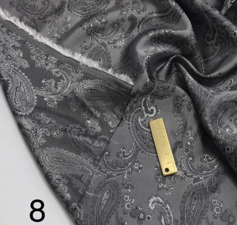 May include: Gray paisley patterned fabric with a silver sheen. The fabric is folded and draped, showing the texture and pattern. The number "8" is visible in the lower left corner of the image.