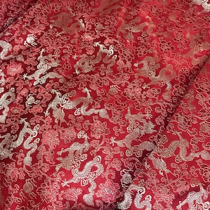 Puede incluir: Tela roja con un patrón de brocado plateado de dragones y flores.