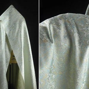 Puede incluir: Una tela verde claro con un sutil estampado floral. La tela tiene una textura suave y sedosa y una sensación de lujo.