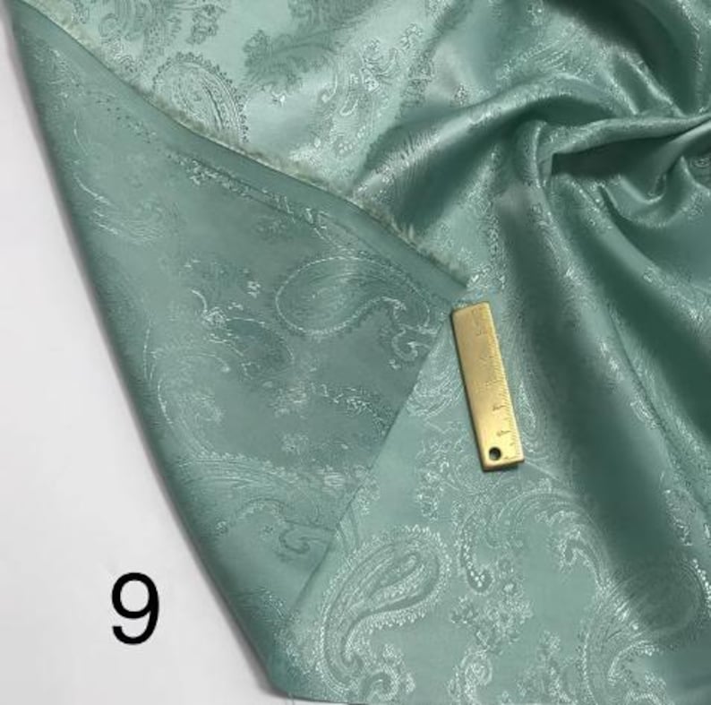 May include: A close-up of a teal paisley patterned fabric. The fabric is folded and has a subtle sheen.