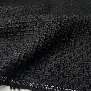 Könnte beinhalten: Nahaufnahme eines strukturierten schwarzen Stoffes mit einem gewebten Muster. Der Stoff hat eine leicht raue, noppige Textur und eine dunkle, einfarbige Farbe. Die Kanten des Stoffes sind ausgefranst und zeigen das Gewebe des Materials.