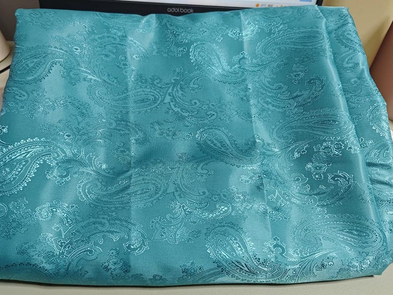 May include: Teal paisley patterned fabric with a satin finish.