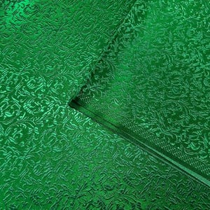 May include: Green fabric with a raised embossed floral pattern. The fabric has a shiny, metallic finish.