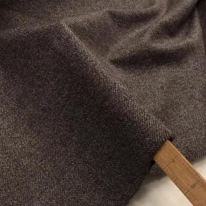 May include: Brown herringbone fabric with a subtle texture. The fabric is folded and draped over a wooden ruler.