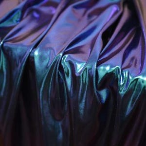 Könnte beinhalten: Nahaufnahme eines irisierenden Stoffes mit einem Farbumschlag von Blau zu Grün. Der Stoff ist glatt und glänzend, mit einem leichten Schimmer.