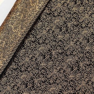 Puede incluir: Tela negra con un patrón floral dorado. El patrón es un diseño repetitivo de flores y hojas estilizadas.