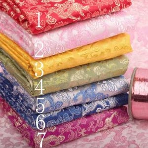 Può includere: Sette tessuti di diversi colori con un motivo a drago. Il tessuto è impilato in una pila con il tessuto superiore rosso e il tessuto inferiore rosa.