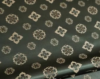 May include: A dark green fabric with a repeating pattern of beige floral designs. The fabric has a subtle sheen and a soft texture.