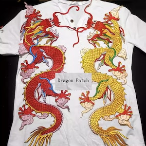 May include: White t-shirt with embroidered dragons in red and gold. The dragons face each other, with detailed embroidery and a text box reading "Dragon Patch". The shirt has a V-neck.