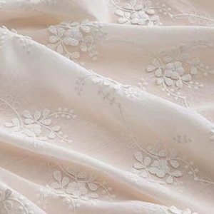 May include: White floral embroidery on a pale pink fabric. The fabric is sheer and delicate, with a soft, flowing texture.