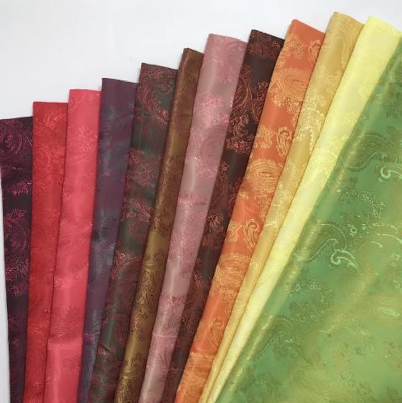 May include: A collection of 12 fabric swatches in various shades of red, orange, yellow, green, brown, and purple. The fabrics have a paisley pattern and a subtle sheen.