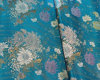 May include: Teal fabric with a white and gold floral pattern. The fabric has a subtle sheen and a textured surface.