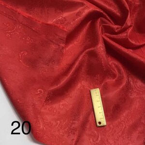 May include: Red paisley patterned fabric with a gold-coloured ruler on top. The fabric has a subtle sheen and a soft texture. The number 20 is visible in the bottom left corner of the image.