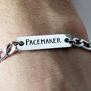 May include: A silver chain bracelet with a silver rectangular tag that reads "PACEMAKER".