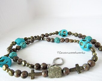 May include: A turquoise and brown beaded necklace with skull and cross charms. The necklace is made with turquoise, brown, and gold beads. The necklace has a silver clasp.