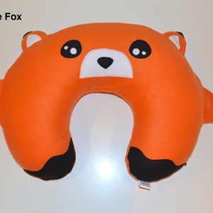 Puede incluir: Almohada de viaje naranja con forma de zorro con orejas, nariz y patas negras. El zorro tiene ojos blancos y una nariz blanca.