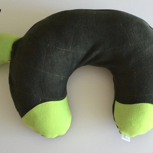 May include: A green and black turtle-shaped travel pillow. The pillow is shaped like a turtle with a green head and feet and a black shell.