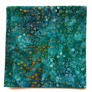 May include: A square piece of fabric featuring a batik-style pattern with various sizes of circles in shades of teal, turquoise, and deep green, accented by scattered golden-brown and bronze circular motifs across the entire surface.