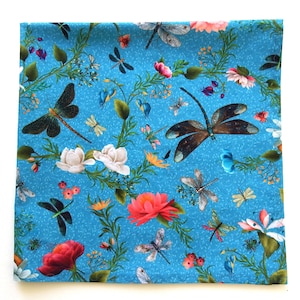 May include: Blue fabric with a repeating pattern of white flowers, pink flowers, and dragonflies. The background is a light blue with a speckled texture.