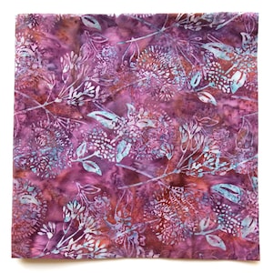 May include: Square fabric with a floral pattern in shades of purple, brown, and teal. The design features stylized flowers and leaves, creating a batik-like effect. The fabric has a soft, textured appearance.