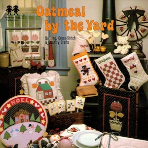 May include: A book titled "Oatmeal by the Yard" with a cover image of a variety of cross-stitch and quilting projects, including a wreath, stockings, and a house. The book is part of the Vanessa-Ann Collection and features quilting, cross-stitch, and country crafts.
