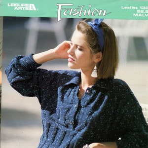 May include: A woman wearing a blue speckled sweater with a button-up collar and a blue headband. She is sitting on a white chair with a metal frame. The sweater has a cable knit pattern and is paired with a plaid skirt. The image is from a knitting pattern booklet titled "Fashion" featuring "nomotta MALVA".